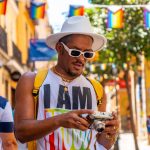 A gay black ethnicity man at the pride party looking at the photos on the camera, LGBT flag