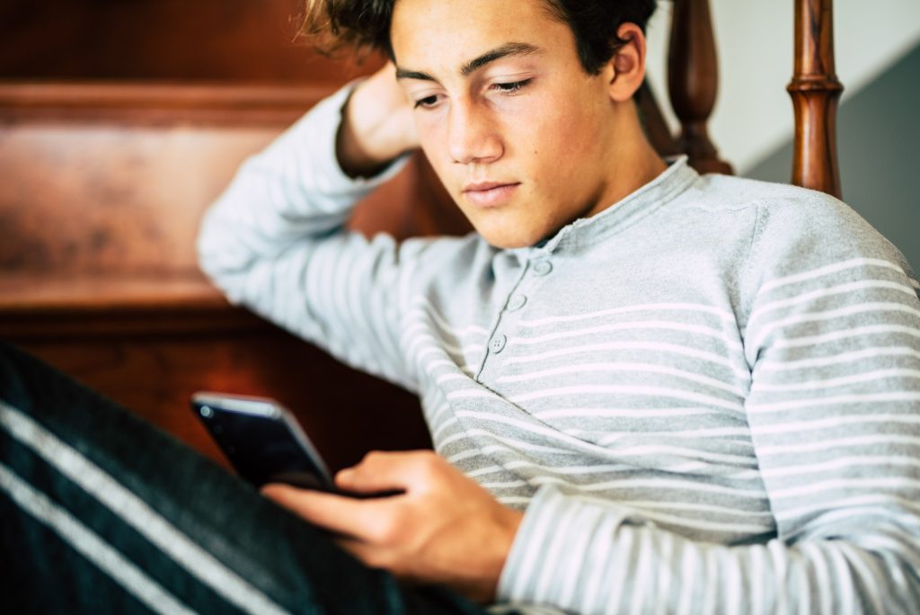 Bored handsome male teenager at home use cellular phone and internet connection