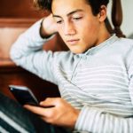 Bored handsome male teenager at home use cellular phone and internet connection