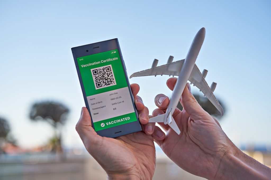 Display with app mobile valid digital green vaccination certificate and airplane toy in hand