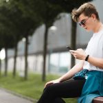 Handsome young guy sitting on a bench with a smartphone on the internet