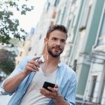 In a great mood. Young man is listening to music via earphones while walking around the city
