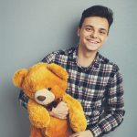 Man holds teddy bear on a light blue background, copy space. Pretty toy concept.