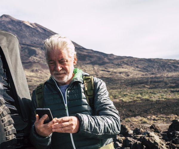 Caucasian old man use modern technology cellular phone at the mountain during trip vacation